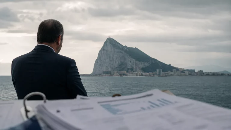Pedro Sánchez y José Manuel Albares sonriendo, con el Peñón de Gibraltar al fondo, simbolizando el acuerdo fronterizo. Composición editorial.