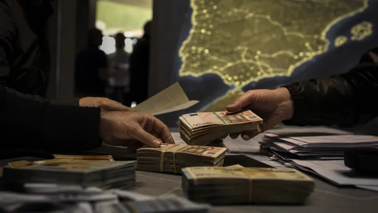 Manos anónimas manipulando pilas de billetes de euros y documentos borrosos, con un mapa estilizado de España y Marruecos de fondo, sugiriendo transferencias opacas y un flujo de dinero no controlado.