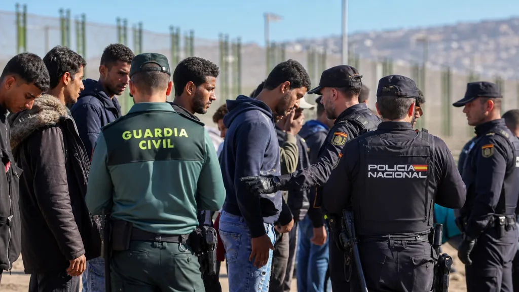 Guardia Civil y Policía Nacional rastreando a recién llegados en Ceuta, con el fondo de la frontera.