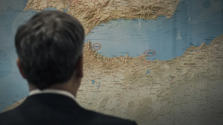 Vista de espaldas de una persona observando un mapa geopolítico de la región del Estrecho de Gibraltar y el norte de África, donde las ciudades de Ceuta y Melilla están destacadas. La escena sugiere un análisis estratégico, con un leve desenfoque en el rostro de la persona.